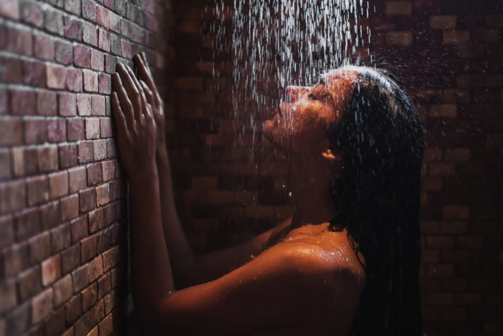 Woman relaxing under hot shower in dark room