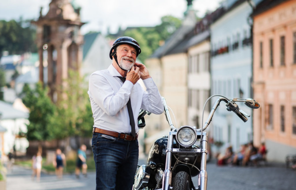A senior businessman with motorbike in town, putting on helmet